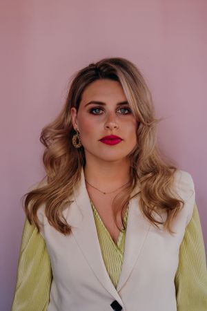 Professionele headshot met gestylede blonde golven, gekleed in een witte blazer en een limoengroene top.