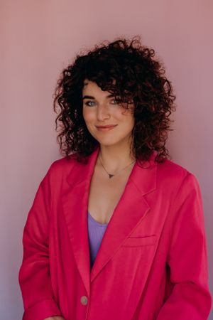 Stijlvol portret van een model in een felroze blazer en een paarse top tegen een roze achtergrond.