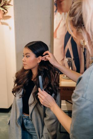Haarstylist gebruikt een krultang op het lange donkere haar van een klant in een salonomgeving.