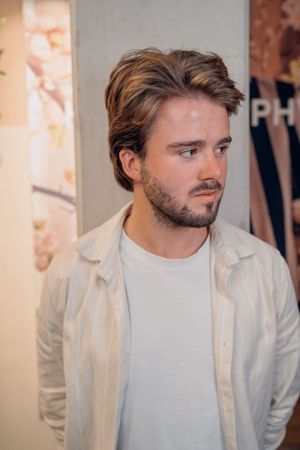 Een persoon gekleed in een witte overhemdblouse en een wit T-shirt poseert voor een neutrale achtergrond.