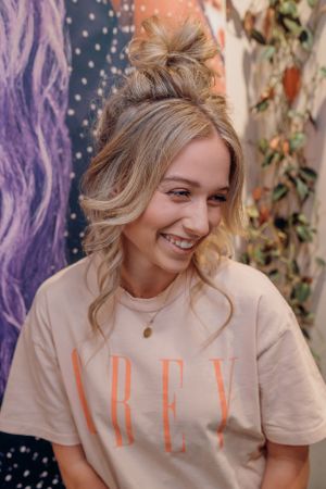 Natuurlijk, spontaan lachend portret met een nonchalante knot, gekleed in een crèmekleurig T-shirt met tekst.