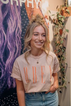 Casual portret tegen een kleurrijke muur, gekleed in een crèmekleurige graphic tee met een nonchalante opgestoken coupe.