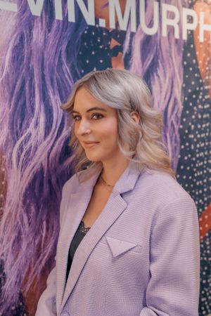 Professioneel portret tegen een paarse achtergrond, gekleed in een lila blazer met golvend blond haar.
