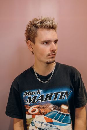 Portret van een persoon in een vintage Mark Martin race-T-shirt met kort geblondeerd blond haar.