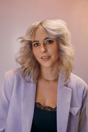 Studioportret in een lavendelkleurige blazer met golvend platinablond haar.