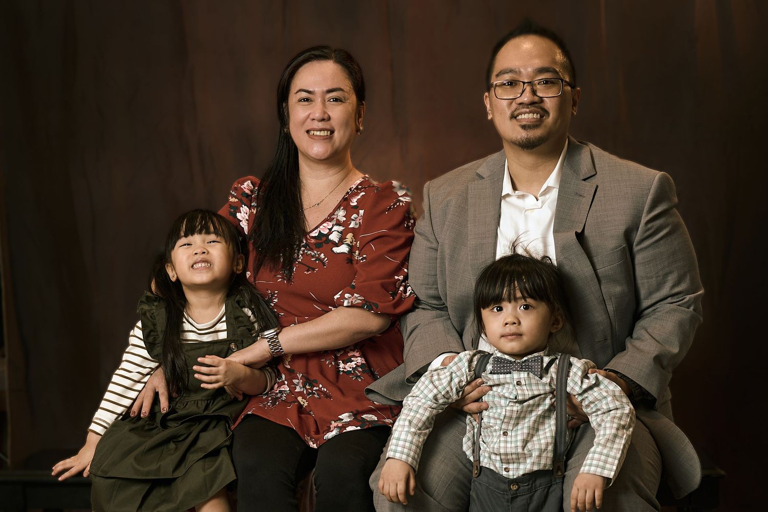 Studio portrait of a family of four against a dark background wearing casual attire.