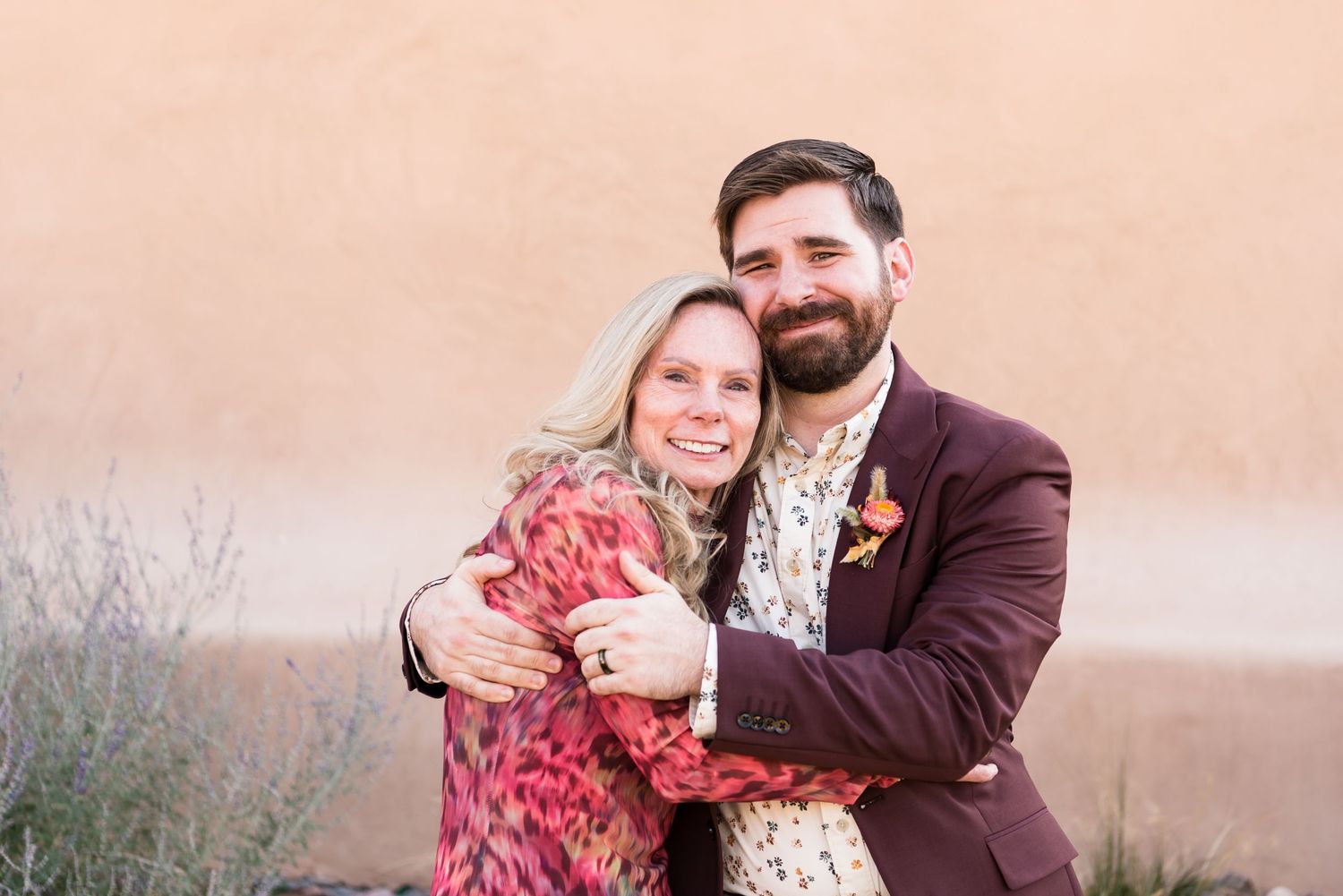 Couple embraces in front of peach colored wall during desert photoshoot.