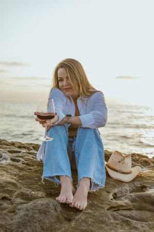 Relaxed beach scene with wine glass and cowboy hat on coastal rocks at sunset.