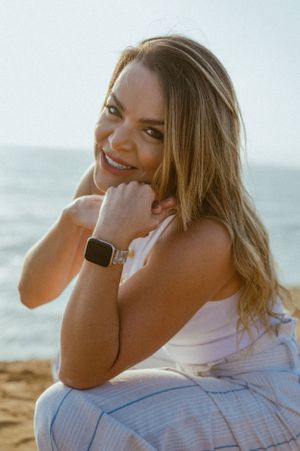 Person in white outfit smiling at the beach during golden hour with smartwatch.