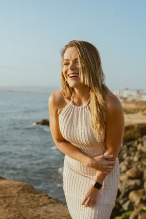 Person wearing beige ribbed dress laughing joyfully by ocean cliffs.