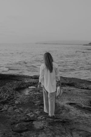 Black and white photo of person looking at ocean from rocky coastline.