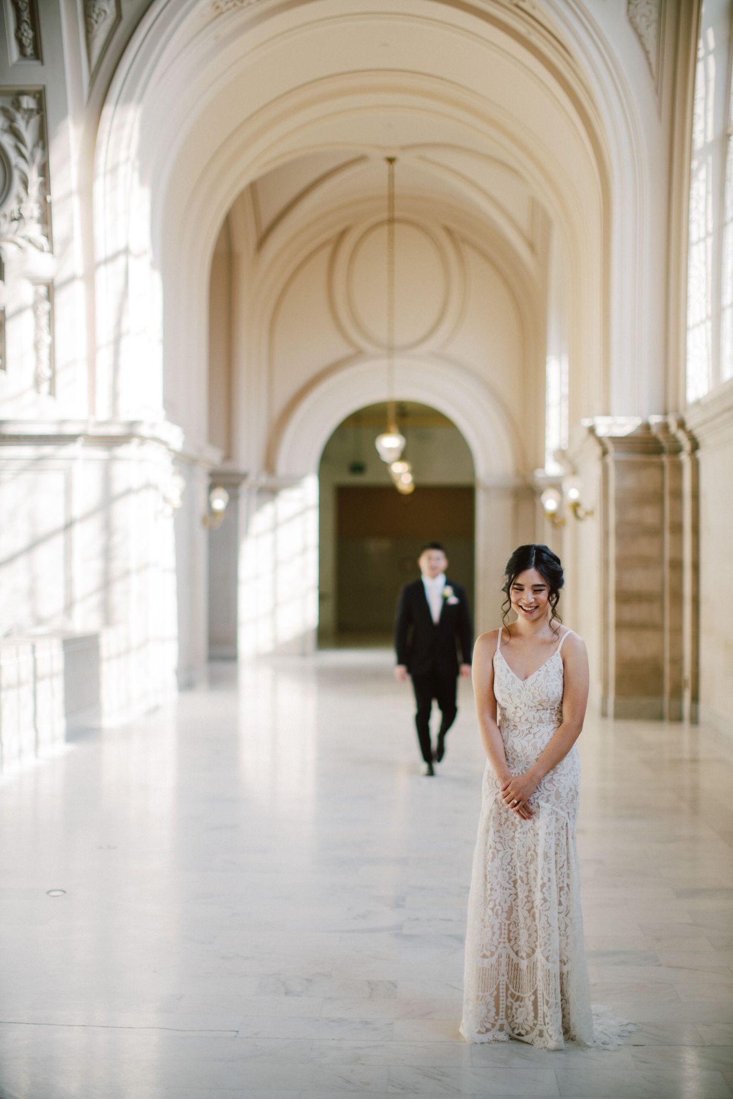 A wedding photo in a majestic white hallway with vaulted ceilings and classical architecture.