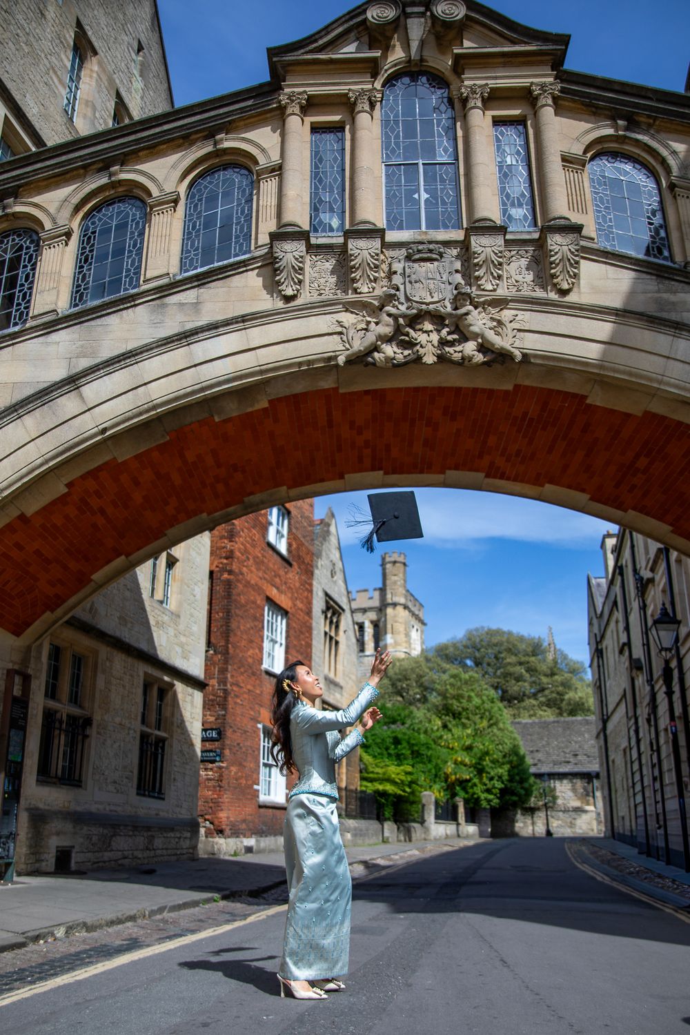 Graduate tossing mortarboard under Bridge of Sighs, Oxford, on a sunny day.