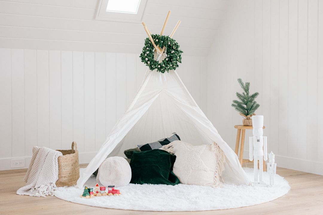 A cozy white teepee tent with Christmas decorations and wreaths in a bright minimalist room.