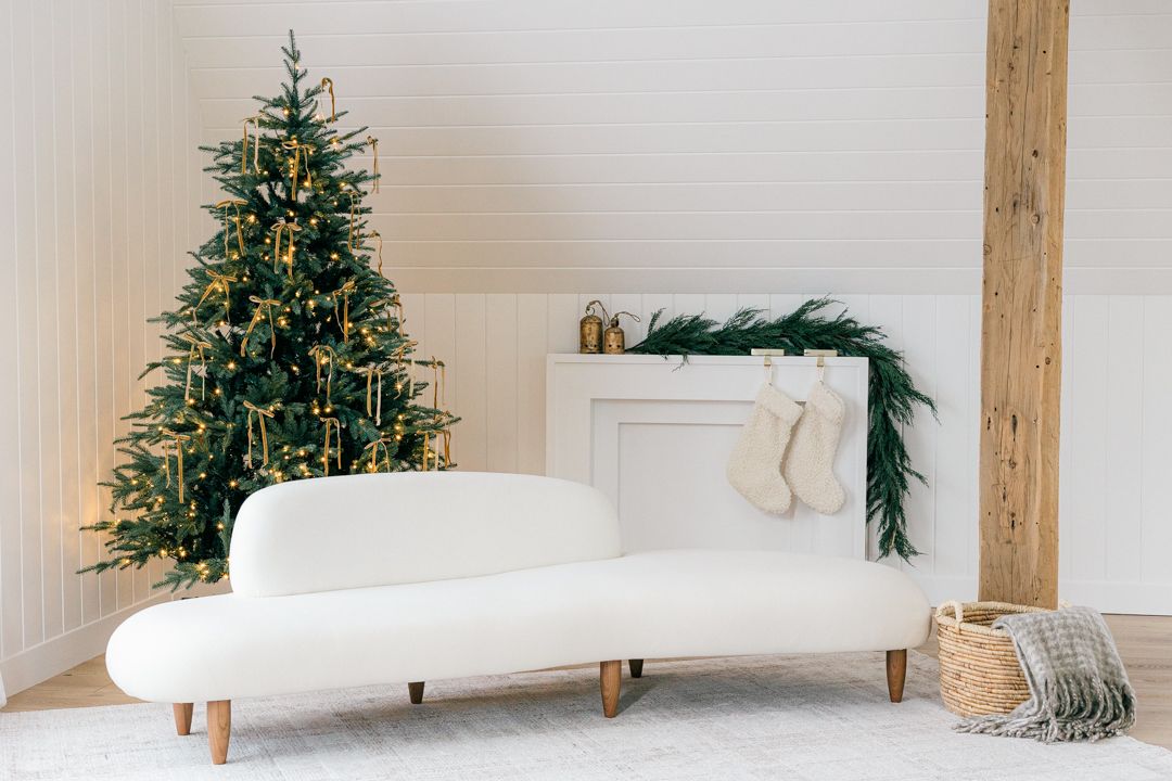 A white modern living room with Christmas tree, curved sofa, and holiday greenery.