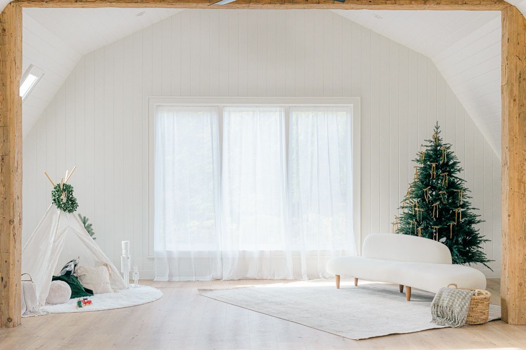 A modern white living room decorated for Christmas with a tree and curved sofa.