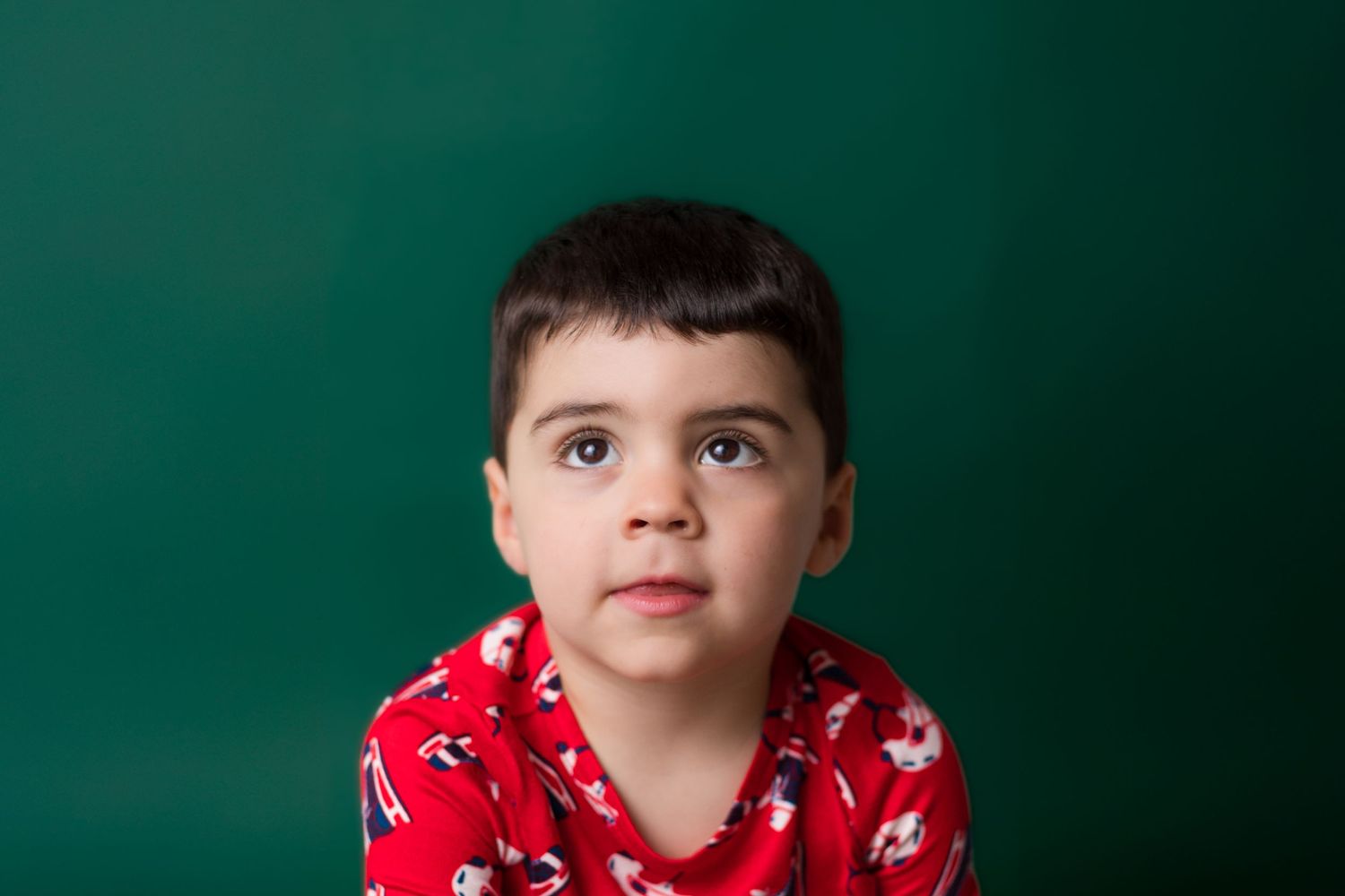 Young child wearing a red and white patterned shirt against a dark green background.