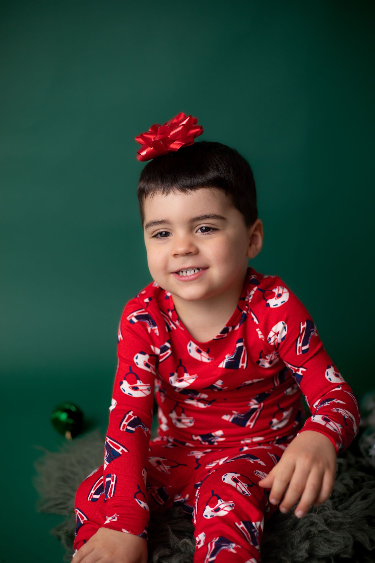A child wearing red patterned pajamas and bow poses for holiday photos against green backdrop.