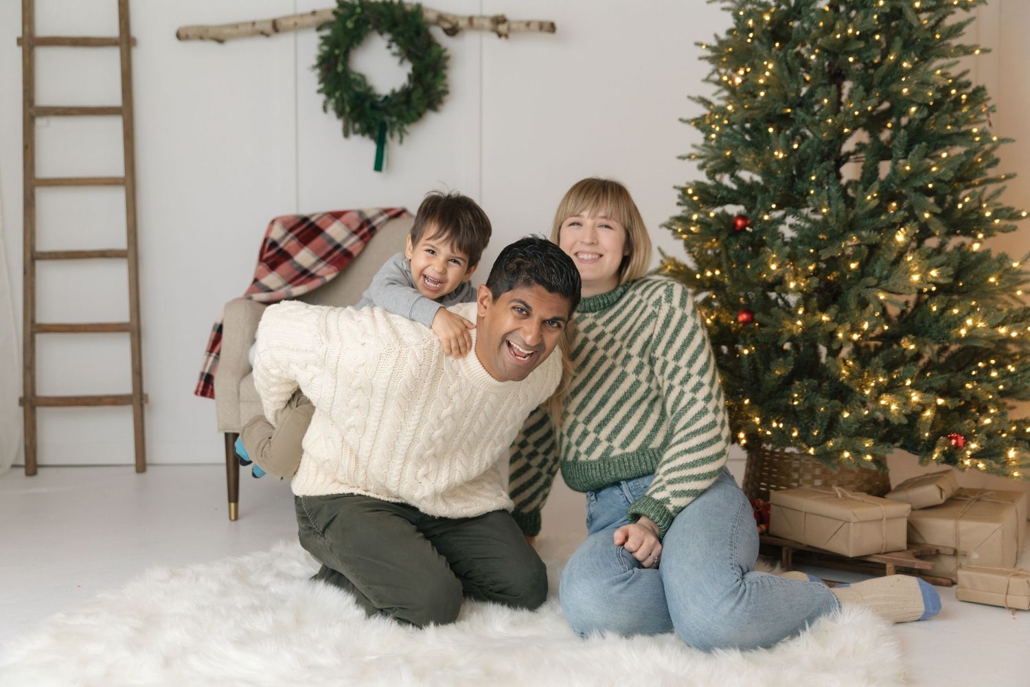 A cozy holiday portrait with warm sweaters and a decorated Christmas tree in the background.