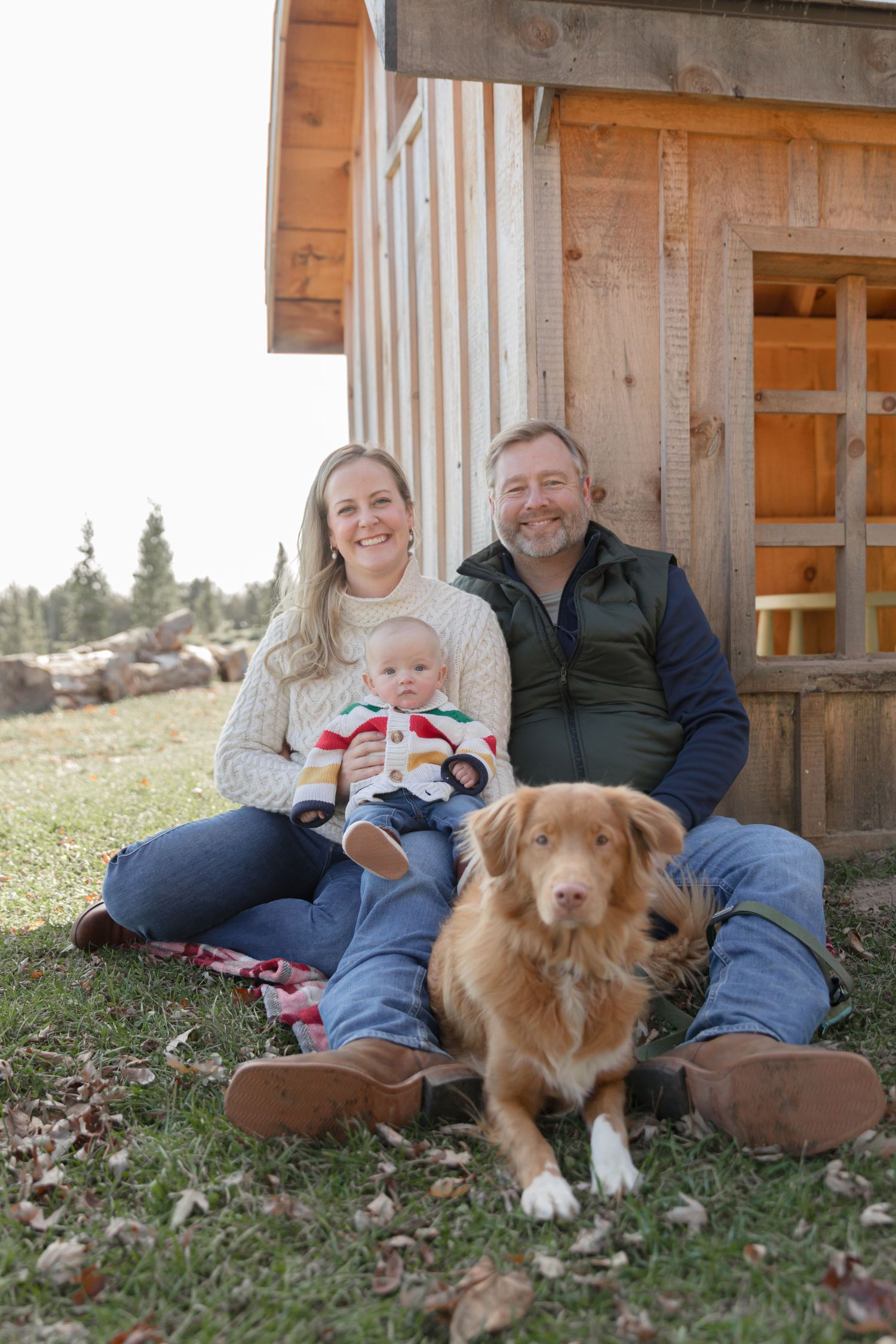 A family relaxes with their golden-colored dog outside a rustic wooden cabin.