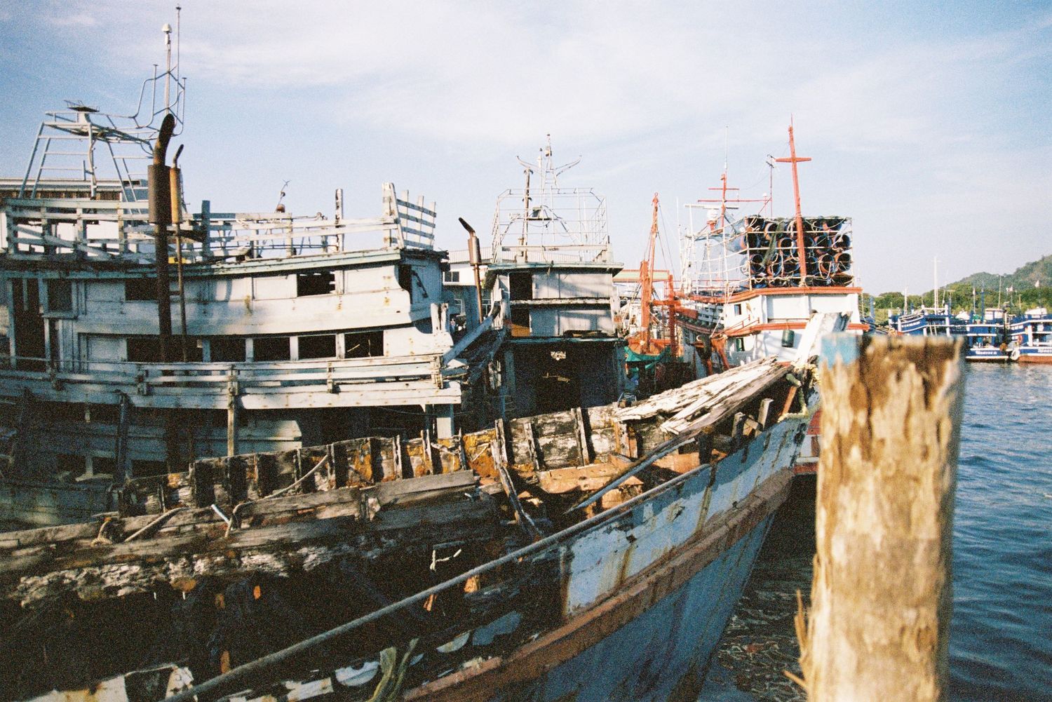 Old weathered fishing boats docked at a busy harbor with rusty equipment visible.