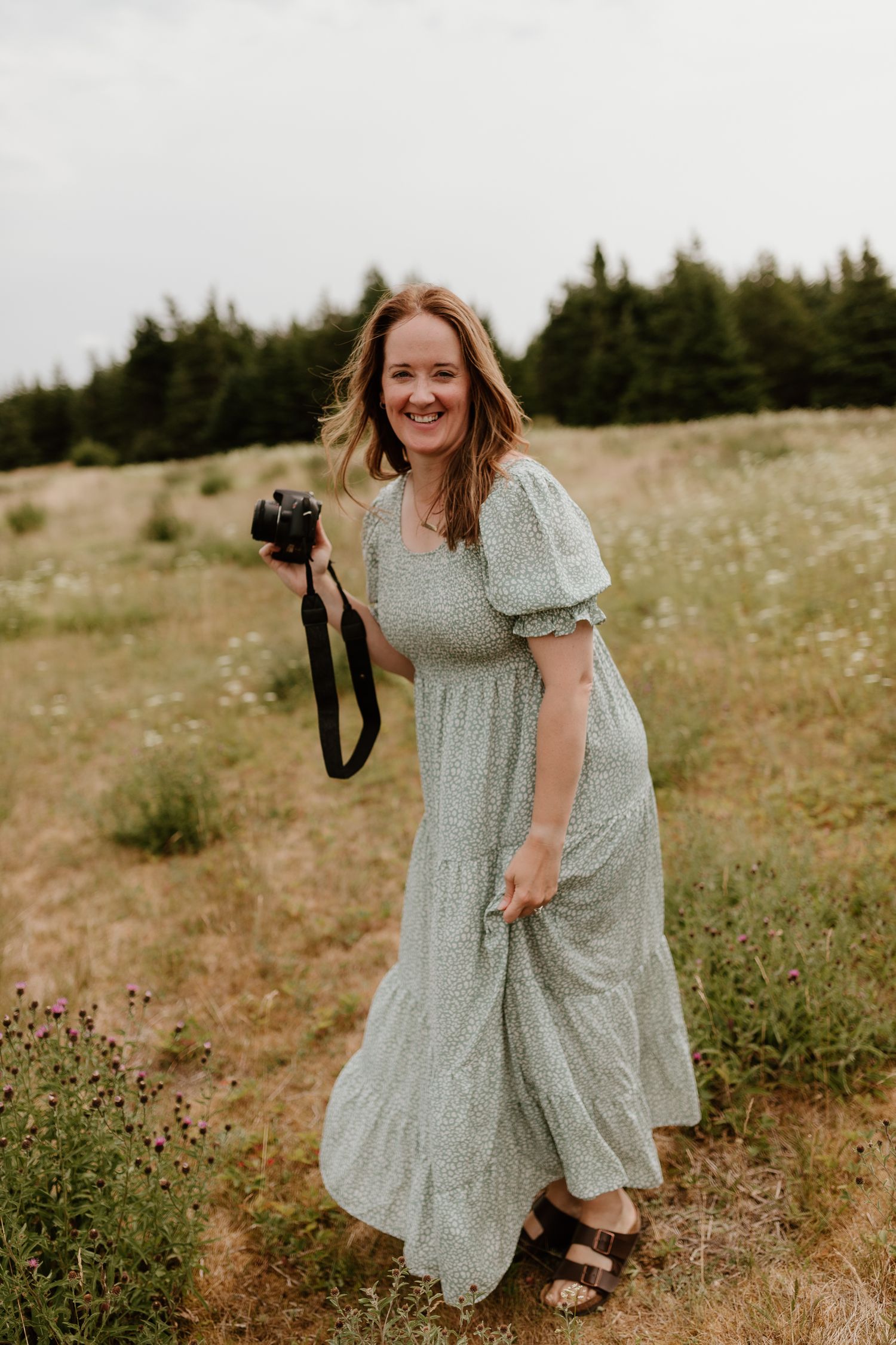 Woman standing in field with a camera in her hand, laughing