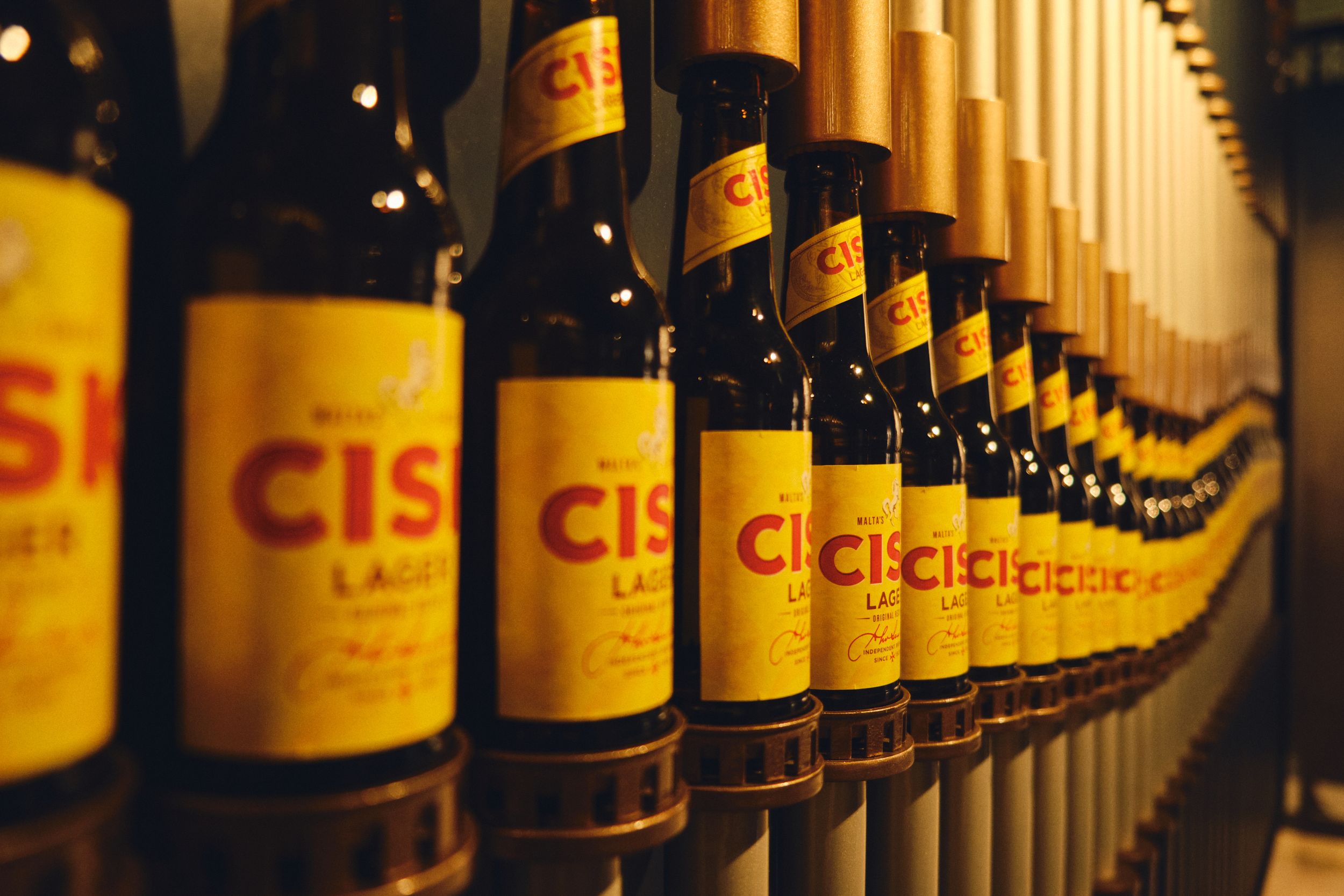 Row of yellow labeled Cisk beer bottles lined up on a shelf.