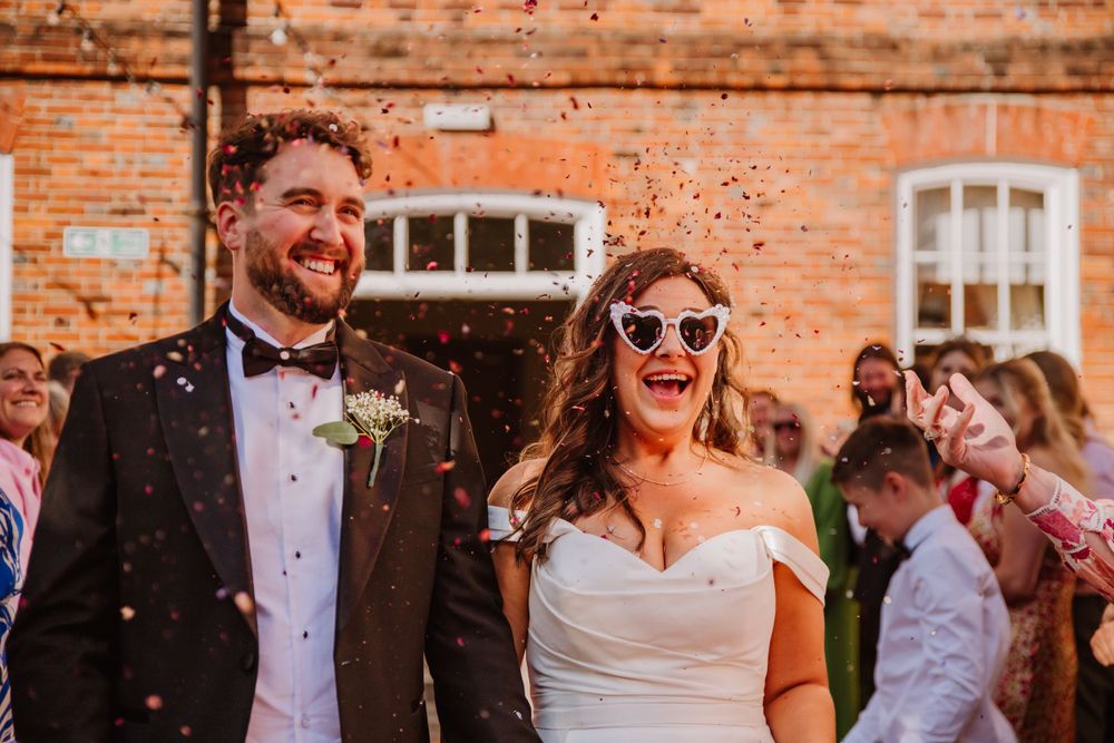 Bride and Groom confetti shot at Hotel Du Vin in Winchester with a golden glow. They are smiling and the bride is wearing heart glasses