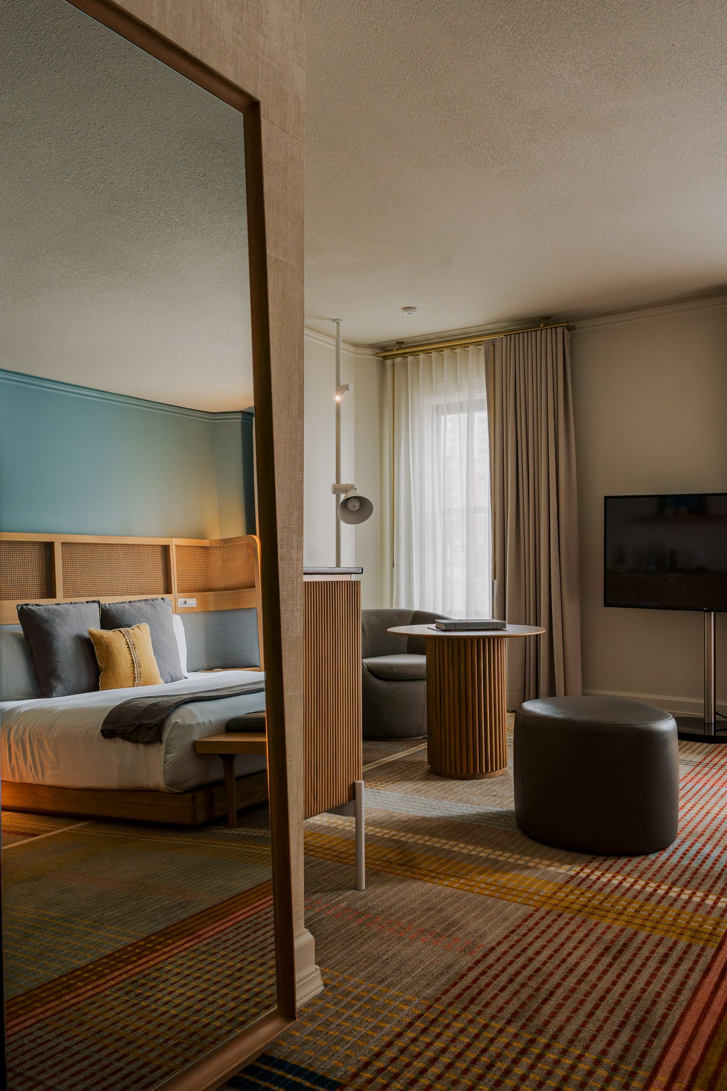 Modern hotel room interior with blue accent wall, large bed, and geometric patterned carpet.