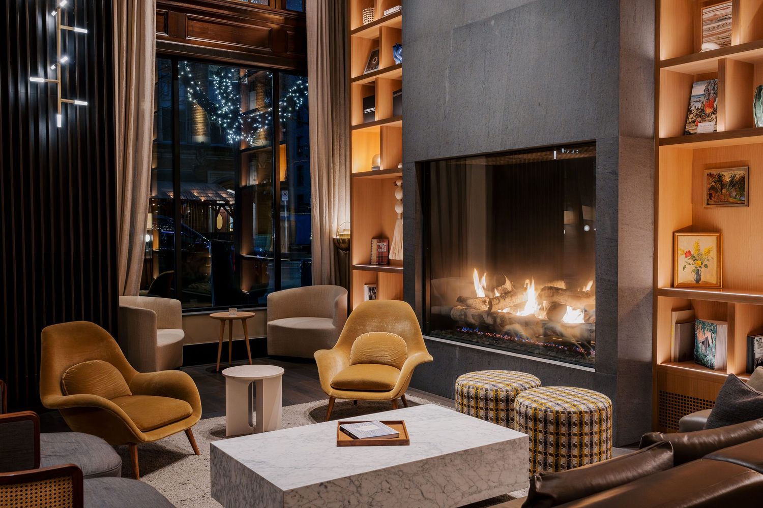 Cozy hotel lounge with modern fireplace, mustard accent chairs, and built-in bookshelves creating a warm ambiance.