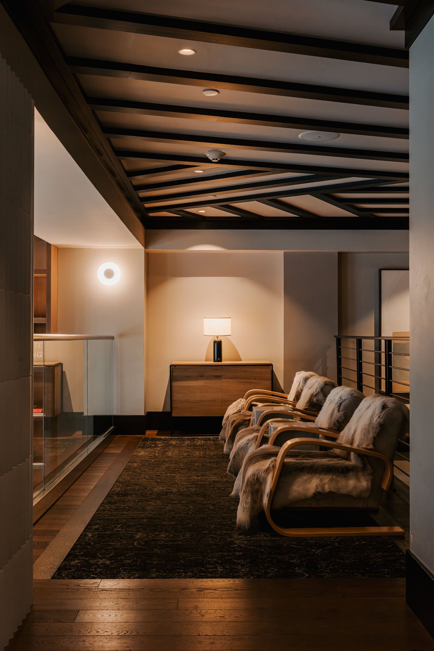 A cozy waiting area with curved wooden chairs and exposed ceiling beams illuminated by warm lighting and wall sconces.