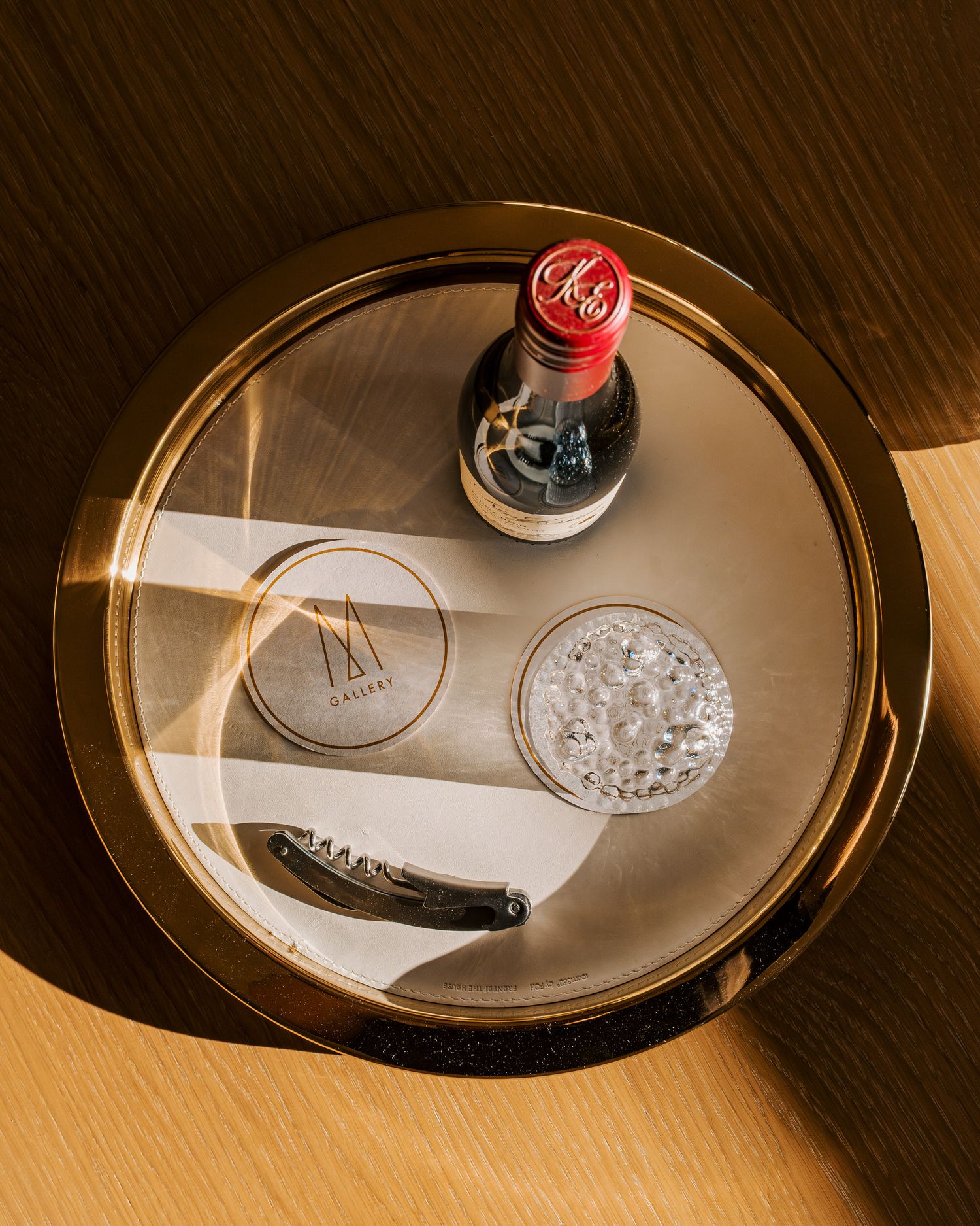 Overhead view of a circular brass tray with a Coca-Cola bottle, glass, and bottle opener in elegant hotel setting.