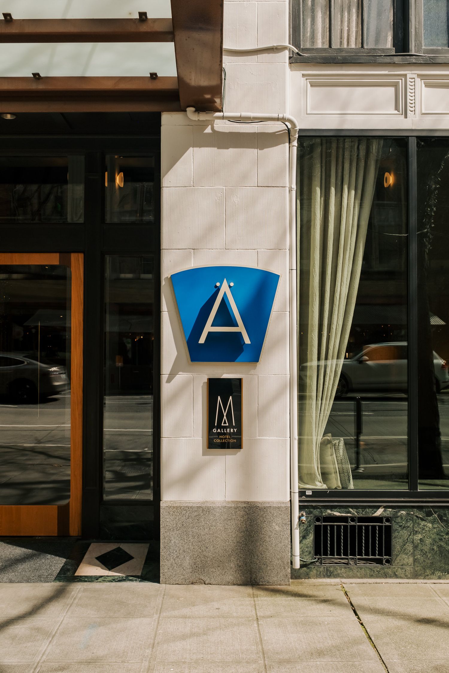 Modern building exterior with blue triangular 'A' sign mounted on white tiled wall between windows and wooden trim.