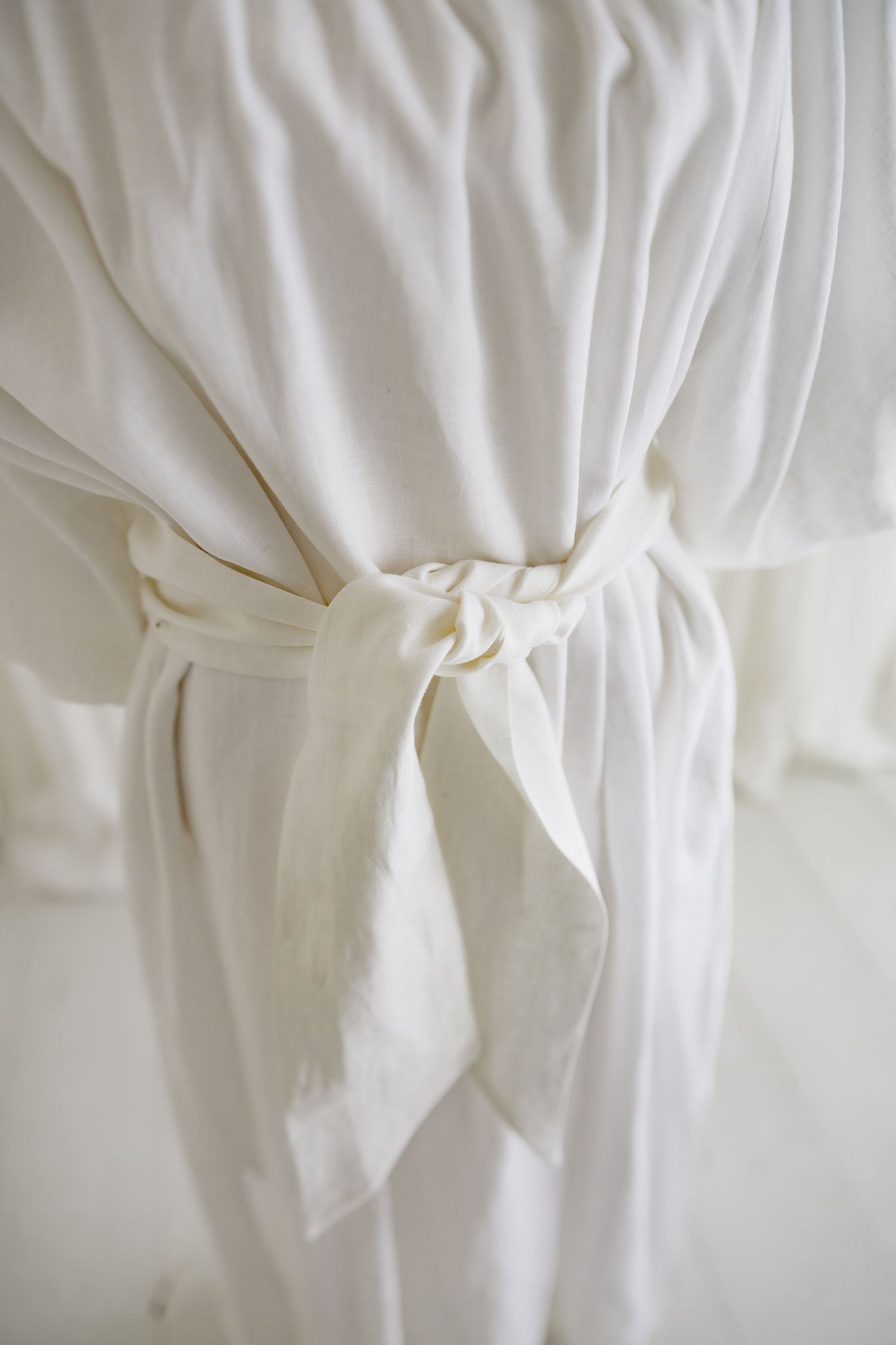Close-up of white fabric belt tied at waist of flowing dress.