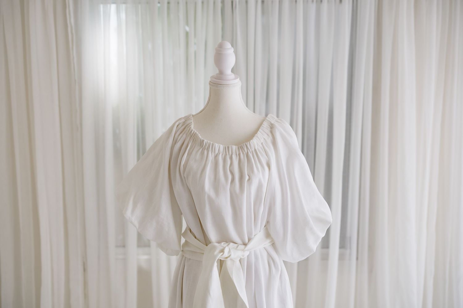White cotton dress with gathered neckline and puff sleeves on display form.