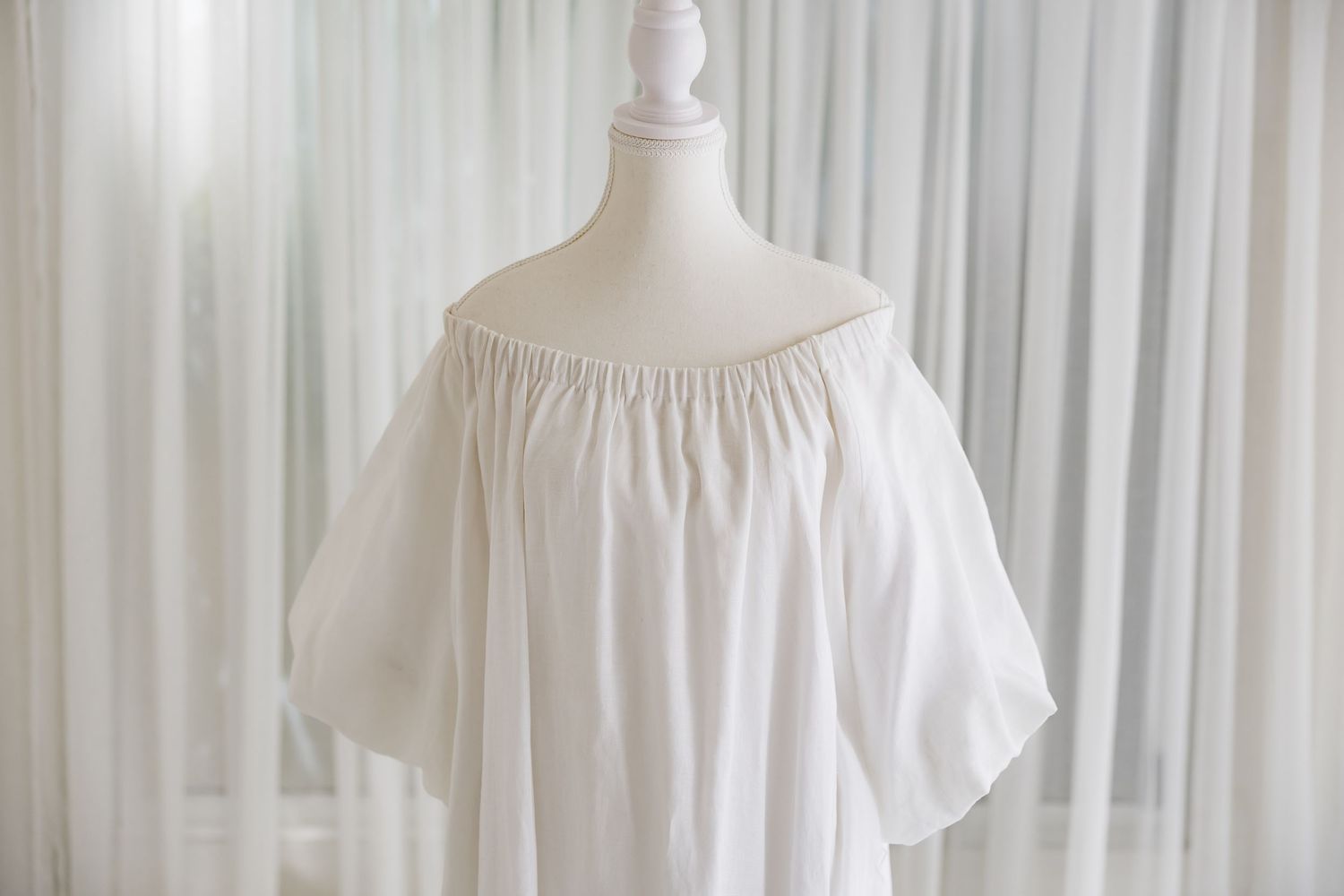 Off-shoulder white dress with elastic neckline shown on mannequin.