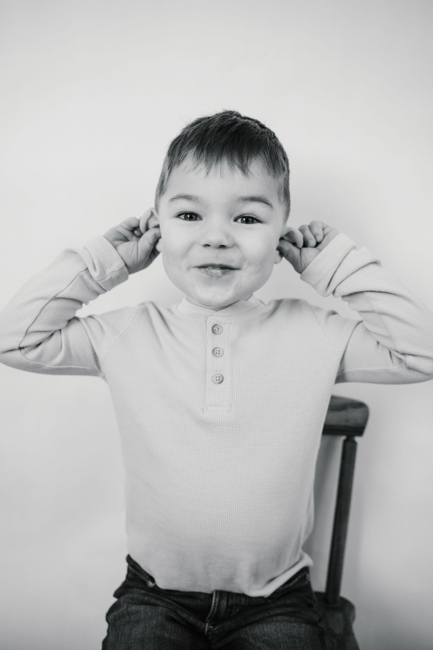 Playful young boy pulling his ears and smiling in a black and white portrait photo.