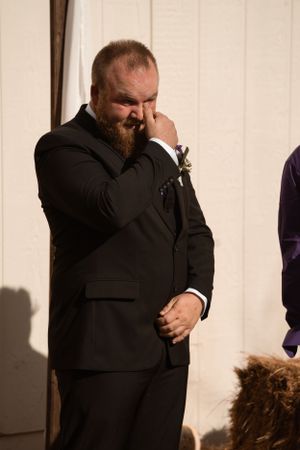 An emotional wedding guest in a black suit wipes tears from his eyes during ceremony.