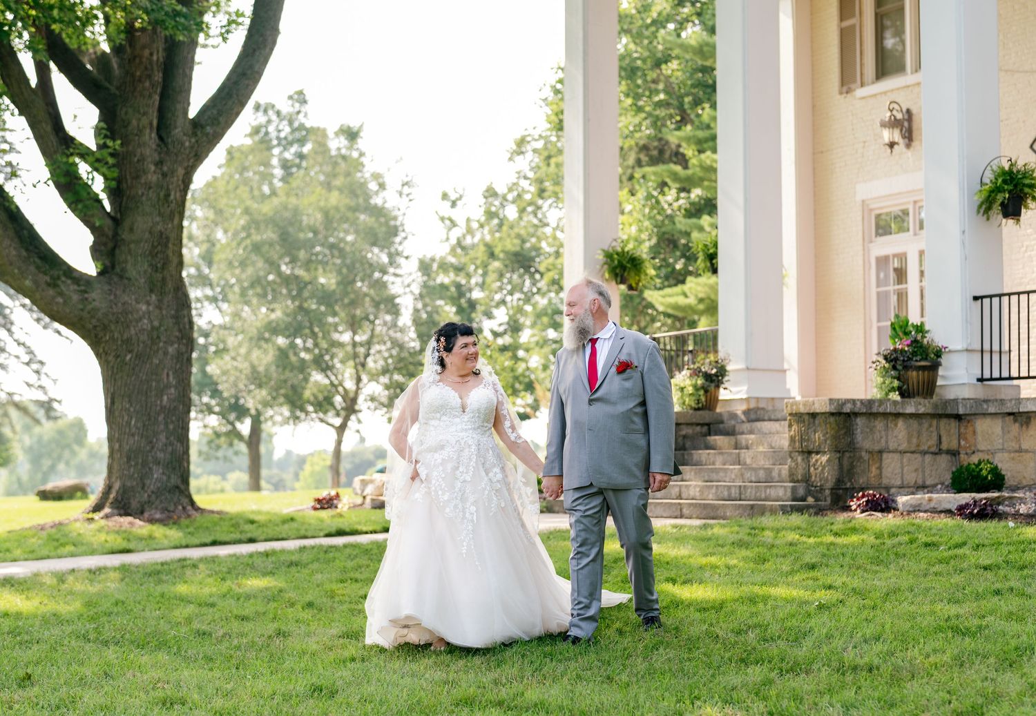 Elegant wedding party poses outdoors on a sunny day with bridesmaids in blue dresses and groomsmen in dark suits.
