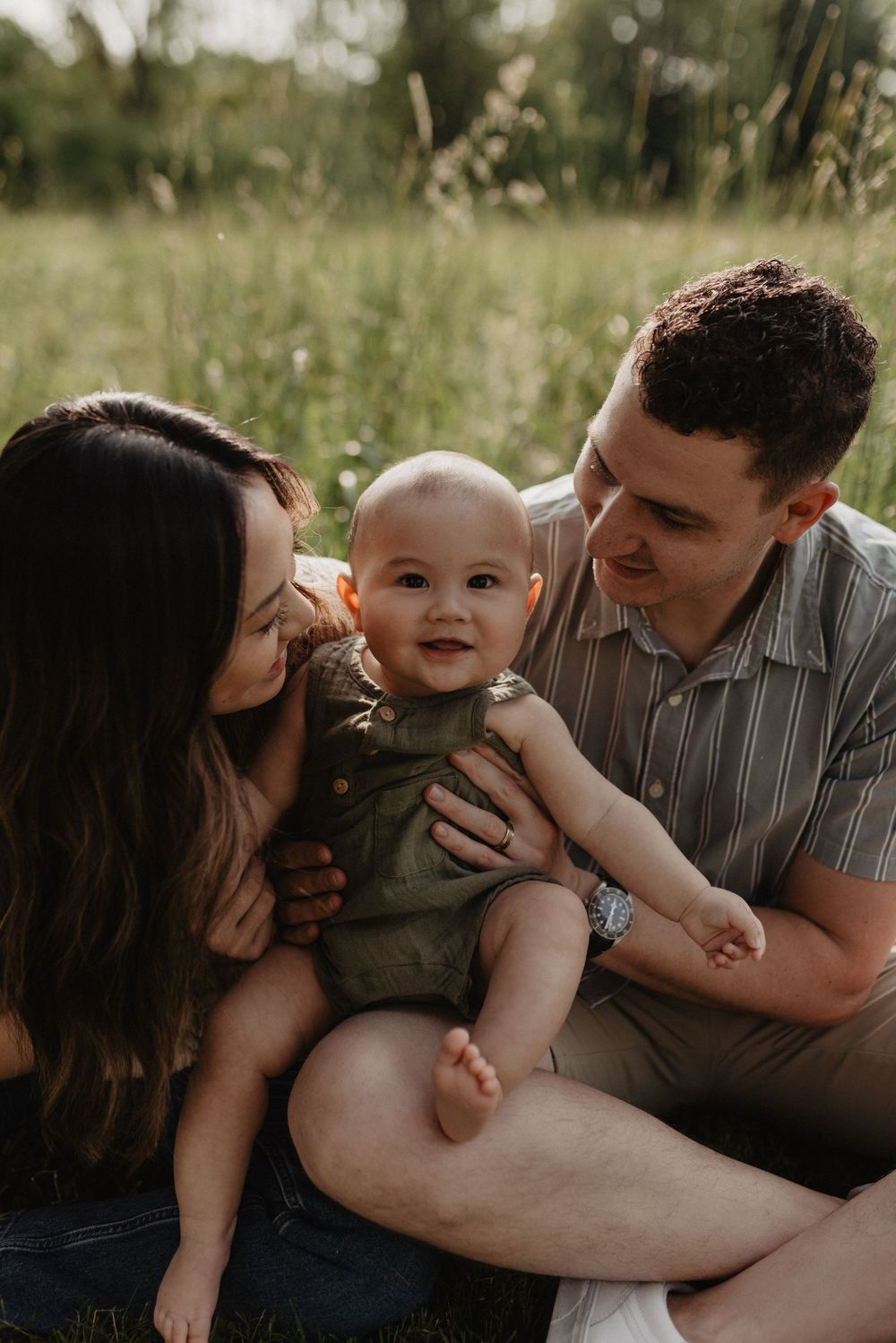 Happy young family with baby sitting in a lush green field at sunset.