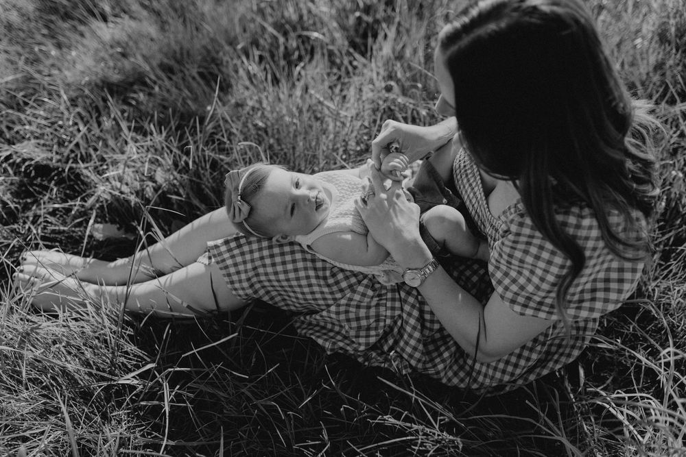 Black and white photo of mother sitting in grass playing with her baby.