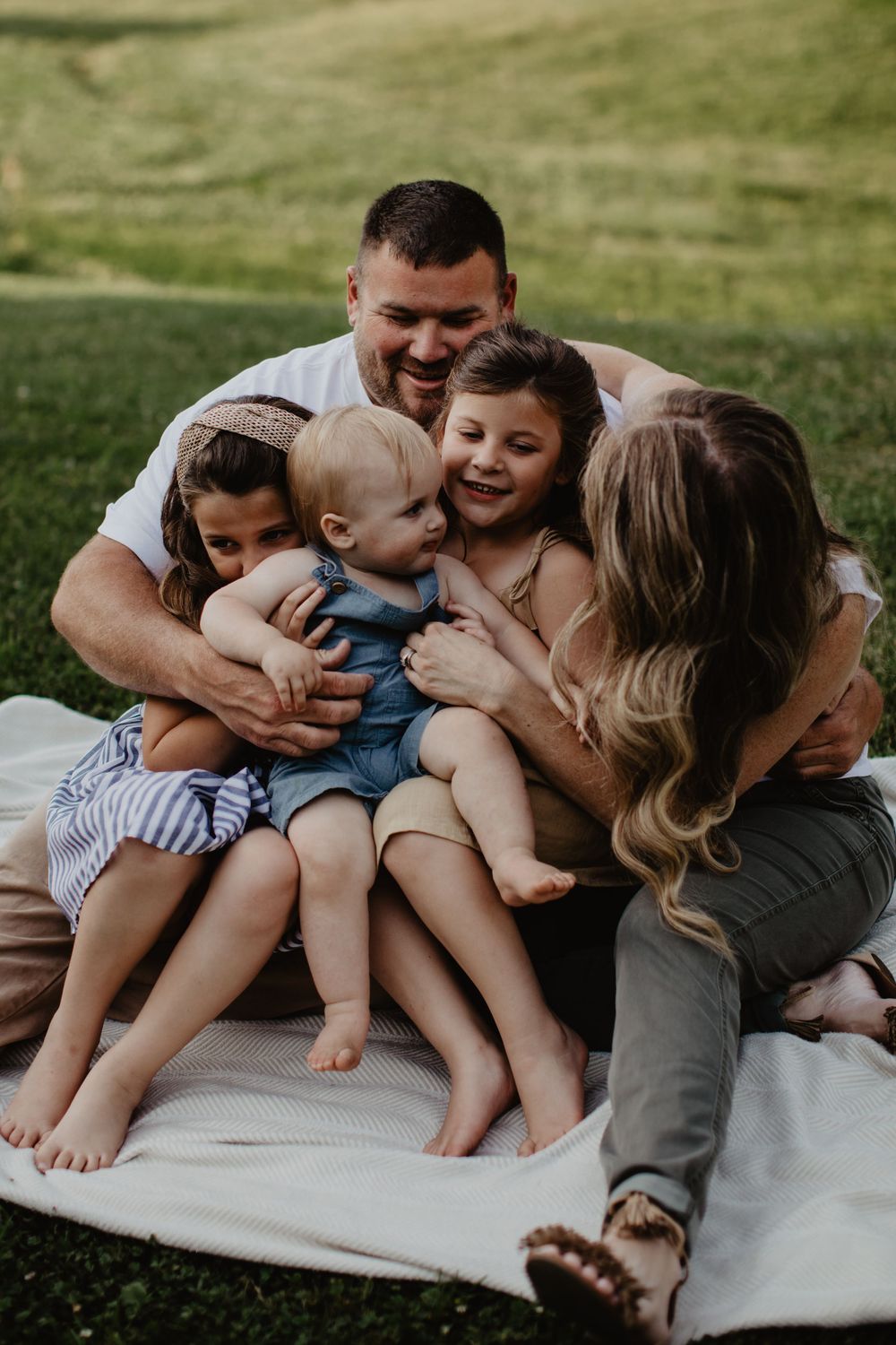 Happy family of six cuddling and laughing together on a blanket in a lush green park.