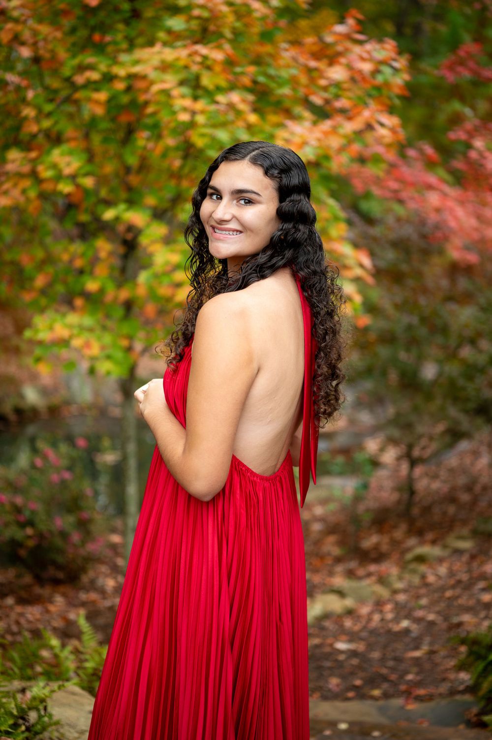 Flowing red backless gown against vibrant autumn foliage background.