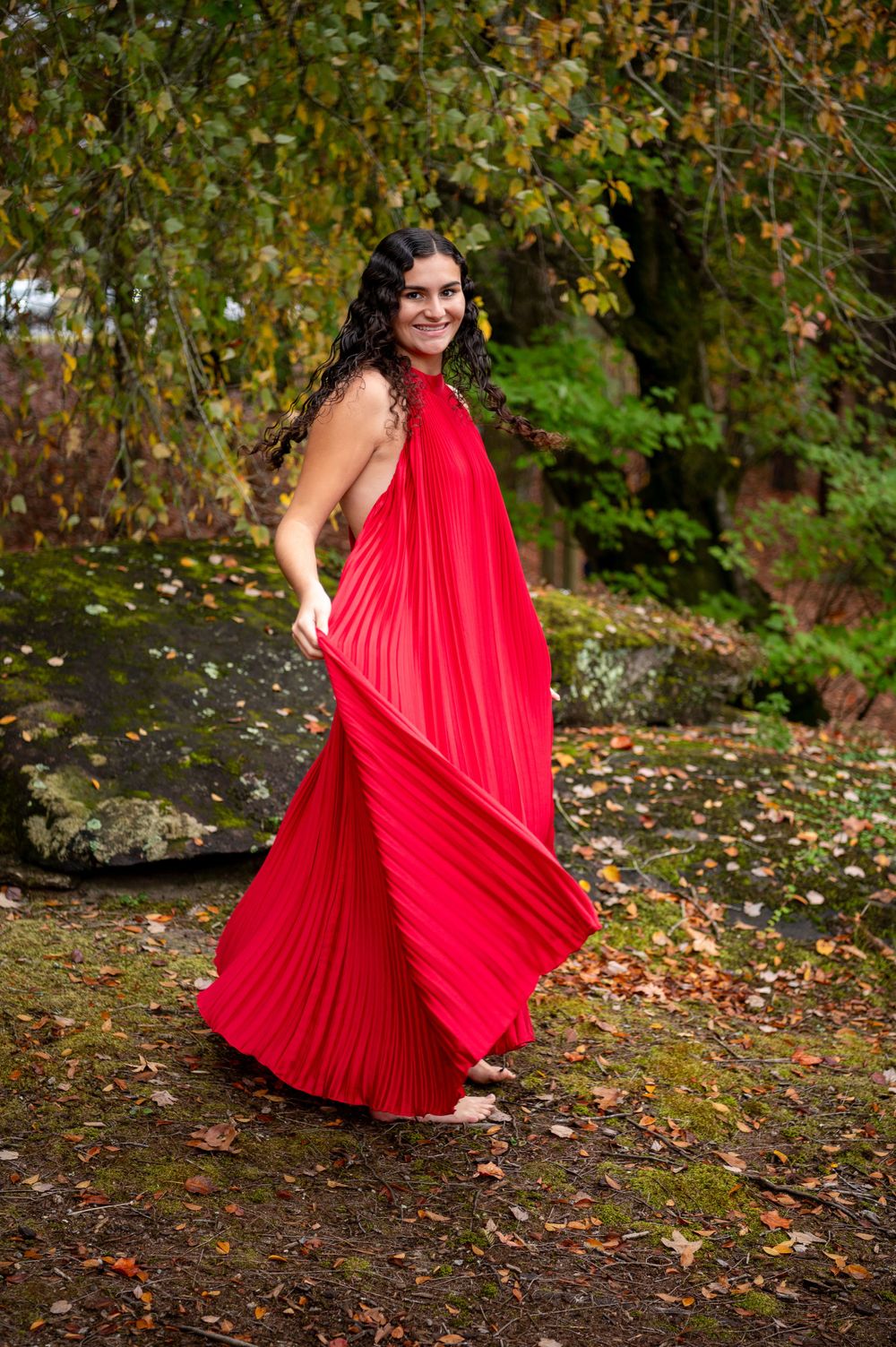 Flowing red pleated maxi dress captured in motion against autumn garden landscape.
