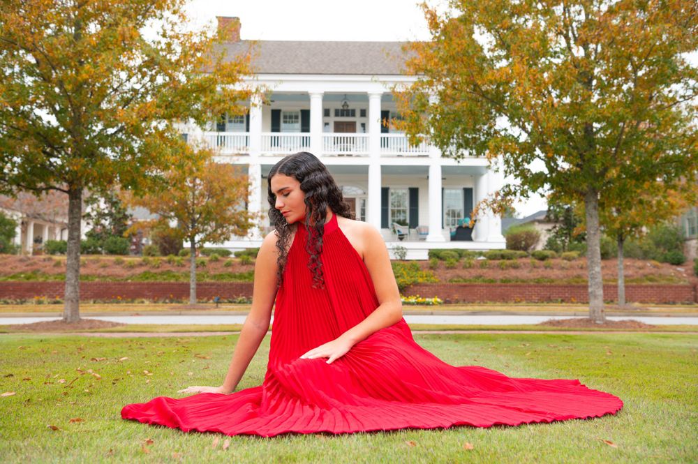 Red flowing dress spread dramatically on lawn with classic white mansion in background.