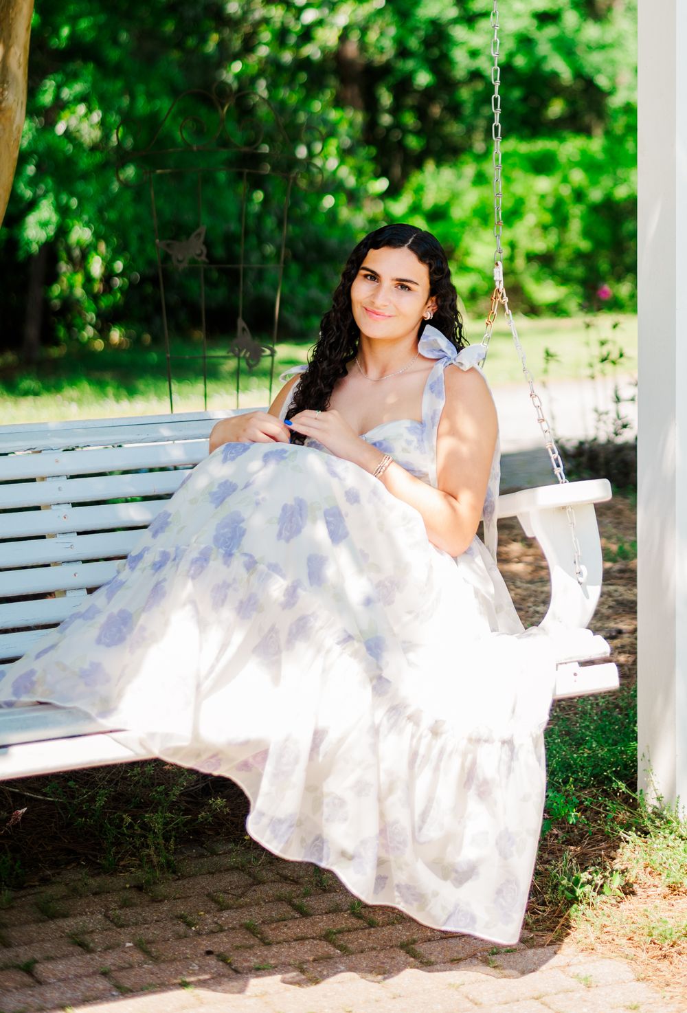 Sitting on a white porch swing in a delicate lavender floral dress surrounded by greenery.