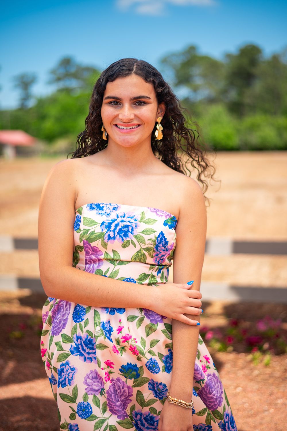 Wearing a strapless floral dress with blue and purple blooms in an outdoor garden setting.