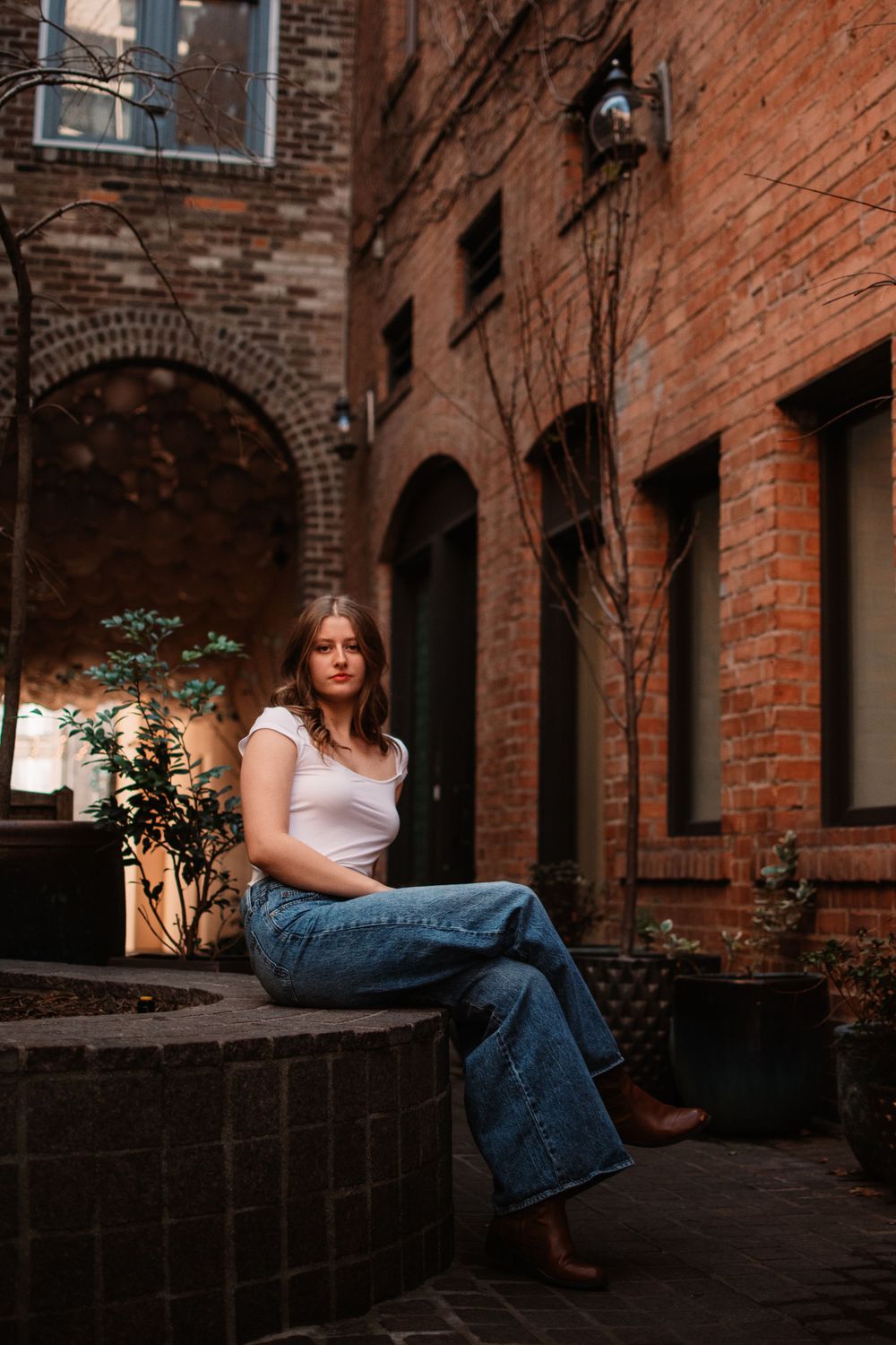 Urban senior portraits in Dallas-Fort Worth with neutral deep tones and a brick backdrop in an alleyway
