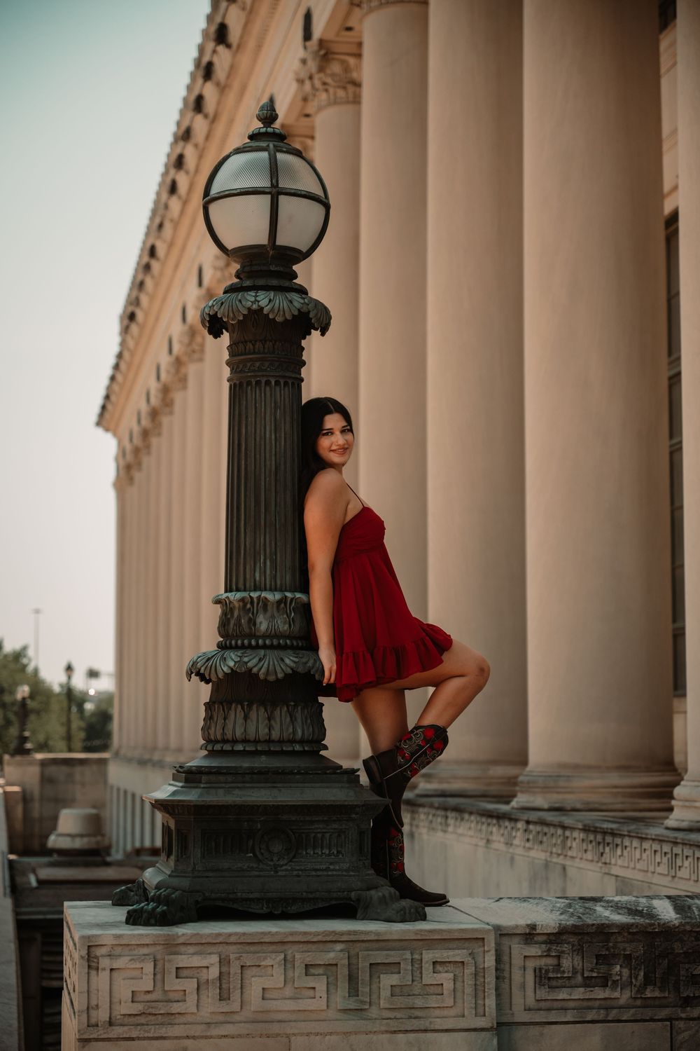 Senior portraits at the Historic Fort Worth post office. Girl wearing a red dress and cowboy boots leaning on lamp post