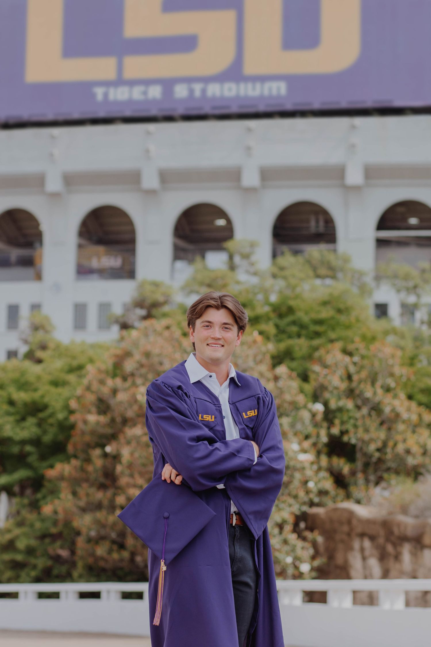 A graduation photo in front of LSU Tiger Stadium featuring purple academic regalia.